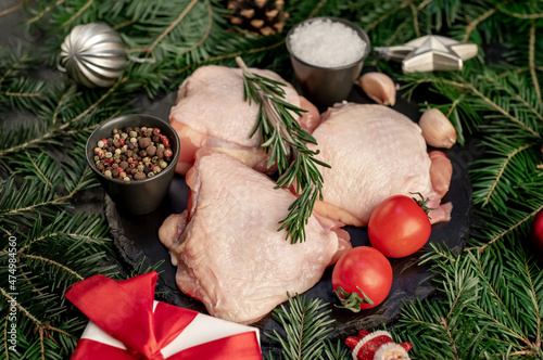 christmas raw chicken thighs with spruce and christmas tree decorations on stone background