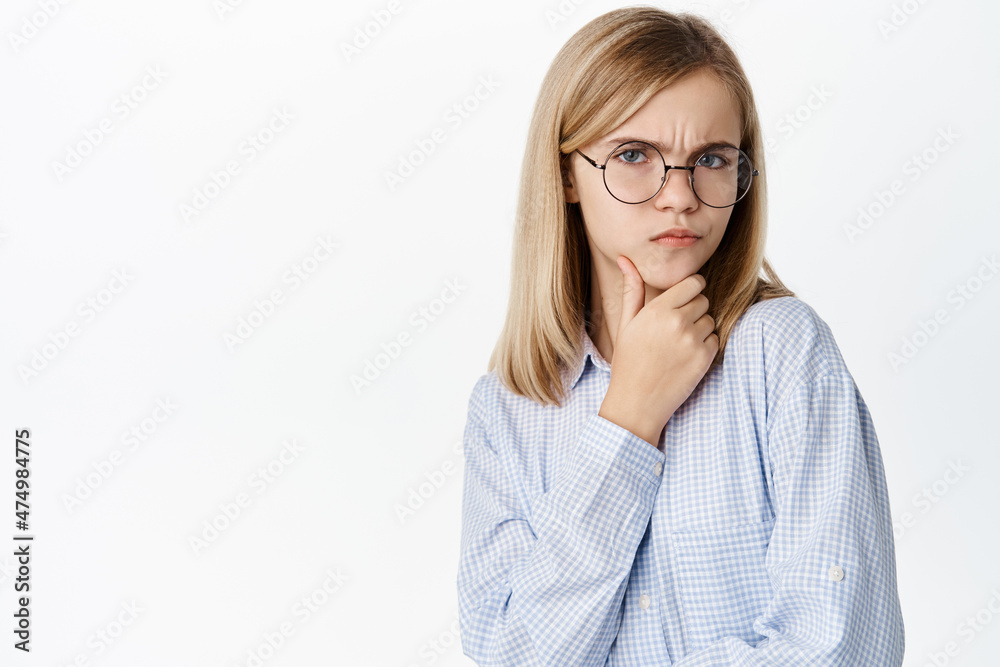 Cute little kid thinking, small girl in glasses pondering, furrow eyebrows and looking thoughtful, standing over white background Cute little kid thinking, small girl in glasses pondering, furrow eyebrows and looking thoughtful, standing over white background