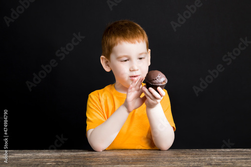 Fototapeta red-haired boy with a delicious chocolate cupcake