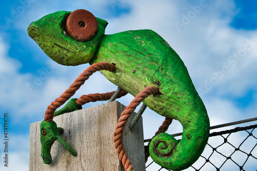 Image of a bright green chameleon, made of driftwood and orange rope. Folk art on a fence near Faro, Algarve, Portugal

