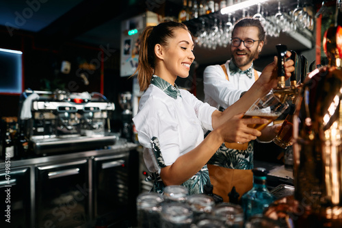 Female bartender pours beer draft beer while working with colleague in bar. photo