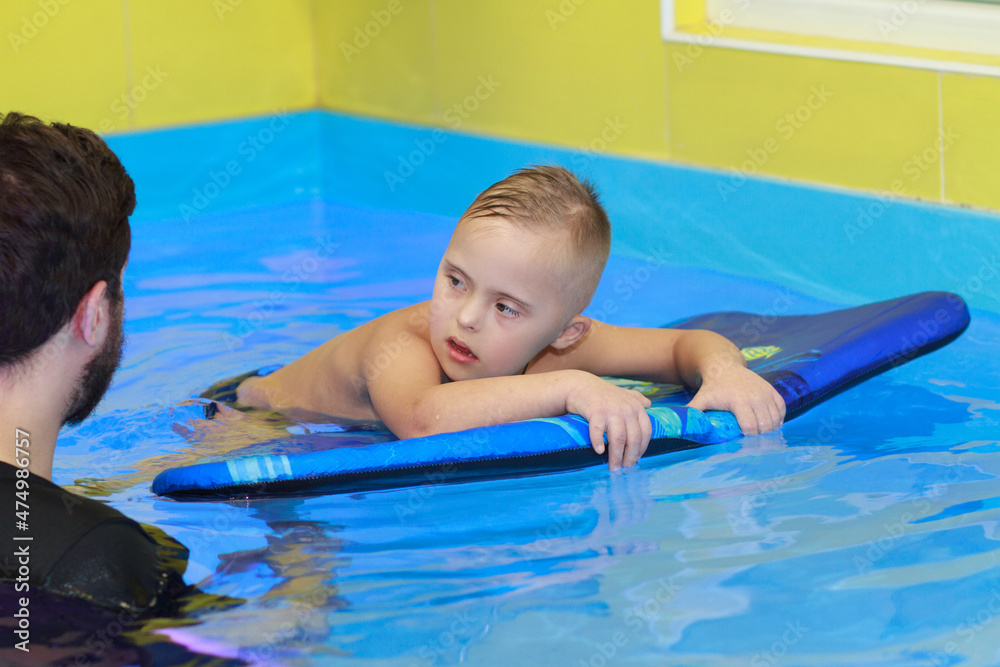 A boy with Down syndrome learns to swim in the pool, rehabilitation of disabled children, genetic anomaly, psychiatric congenital disease.
