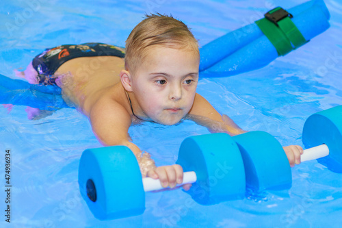A boy with Down syndrome learns to swim in the pool, rehabilitation of disabled children, genetic anomaly, psychiatric congenital disease.
