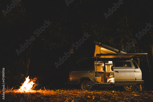 camping concept with camper van and fire at night under the tree in the forest mountain field