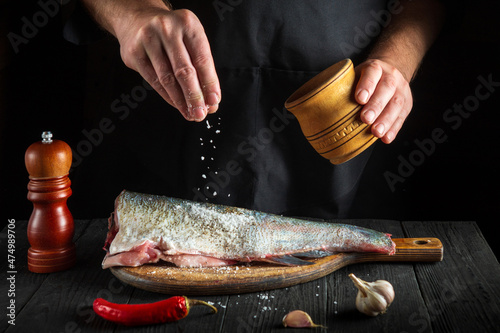 The cook prepares fresh fish sprinkling salt. Preparing to chef fish food. Working environment in the restaurant kitchen photo