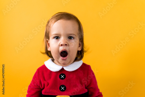 Portraite Emotion Cute Happy Cheerful Chubby Baby Girl in Santa Suit Yawns As If Singing At Orange Background. Child Christmas Scene Celebrating Birthday. Kid Have Fun Spend New Year Time Copy Space
