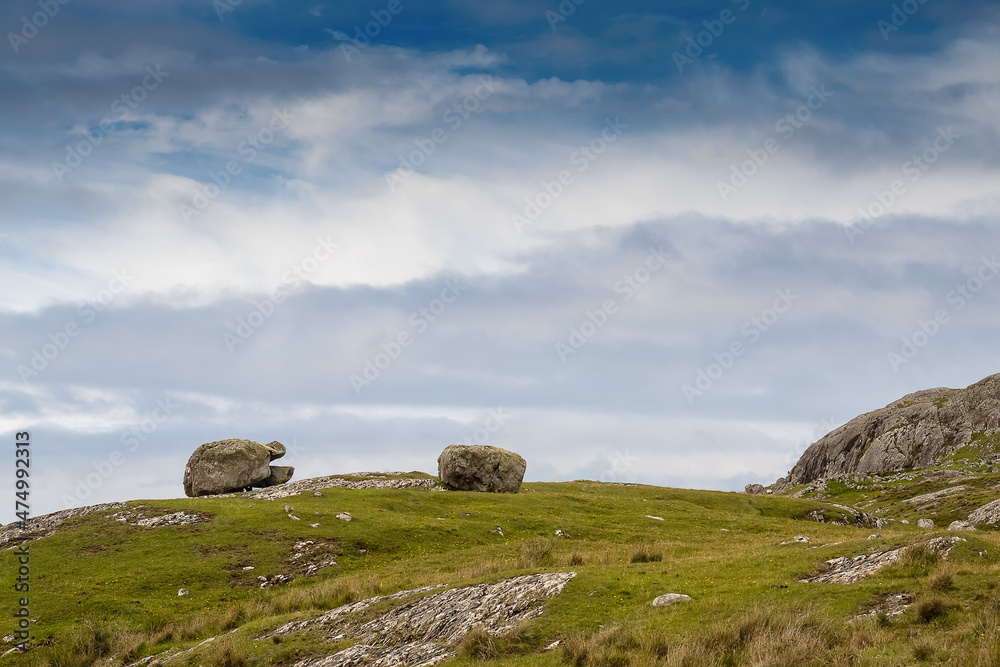 Big rocks on a green grass field, blue cloudy sky in the background. Irish rural landscape scene. County Mayo, Ireland.