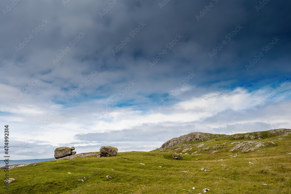 Big rocks on a green grass field, blue cloudy sky in the background. Irish rural landscape scene. County Mayo, Ireland.