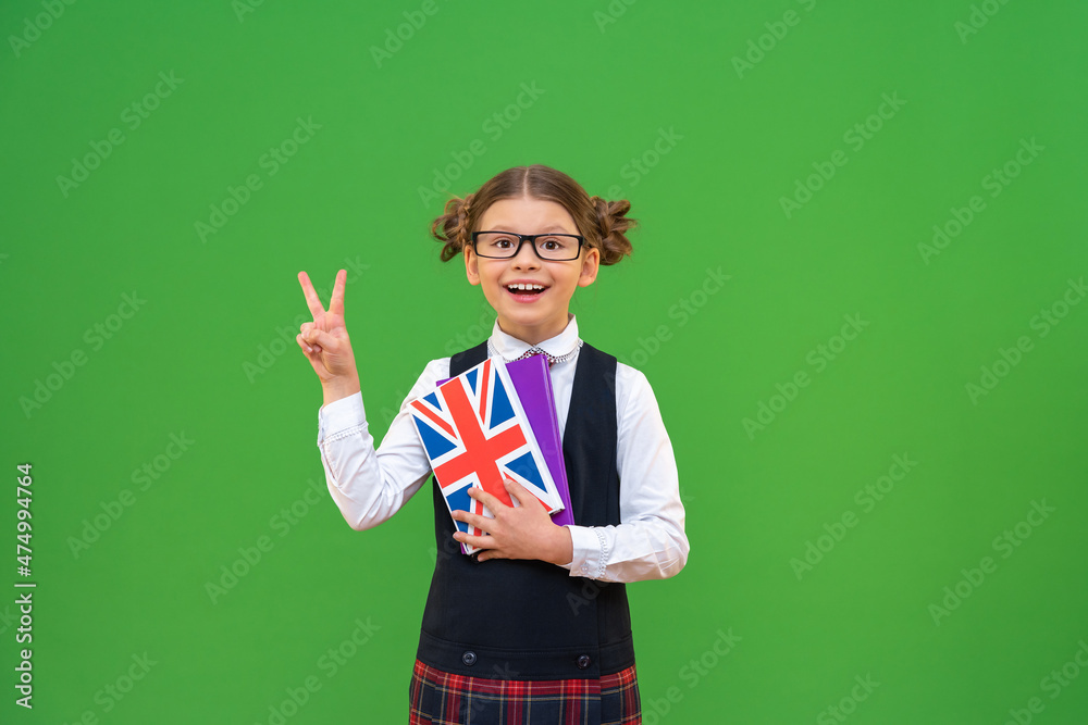 a cheerful schoolgirl with an English textbook in a school uniform with a tie. The student shows two fingers on a green isolated background and copies the space. learning foreign languages, a cheerful schoolgirl with an English textbook in a school uniform with a tie. The student shows two fingers on a green isolated background and copies the space. learning foreign languages,