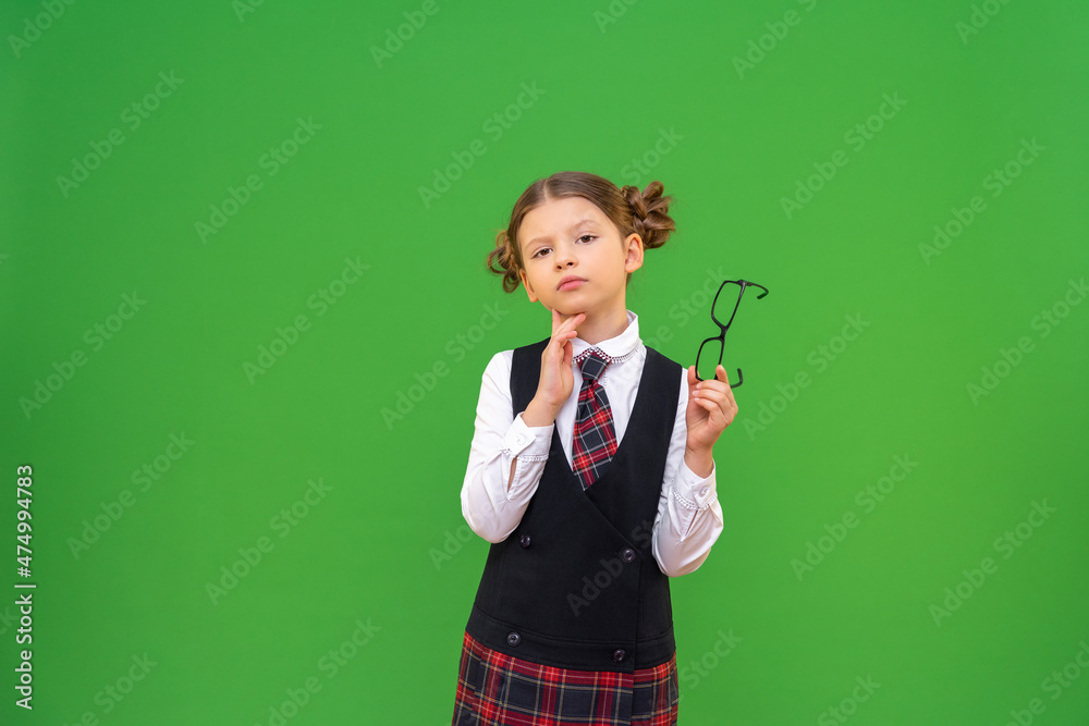 The schoolgirl looks thoughtfully into the camera. a student with glasses and a school uniform on an isolated background. copy space. The schoolgirl looks thoughtfully into the camera. a student with glasses and a school uniform on an isolated background. copy space.