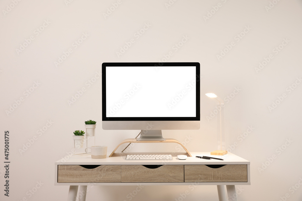Comfortable workplace with blank computer display on desk near light wall. Space for text
