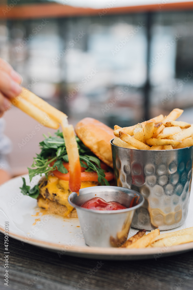 hand dipping French fries into ketchup at outdoor restaurant