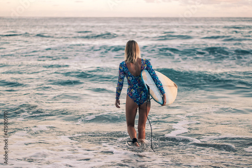 Photography Portrait of blond surfer girl with white surf board in blue ocean pictured from