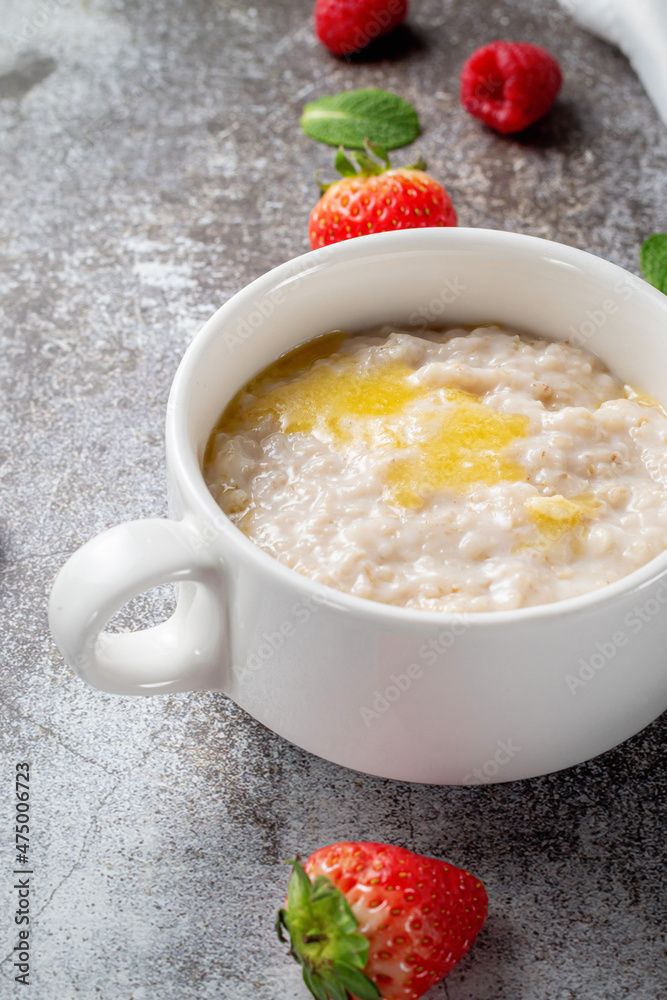 Oatmeal with butter and fresh raspberries and strawberries with mint in a white cup against a gray stone table. A healthy breakfast in a restaurant Oatmeal with butter and fresh raspberries and strawberries with mint in a white cup against a gray stone table. A healthy breakfast in a restaurant