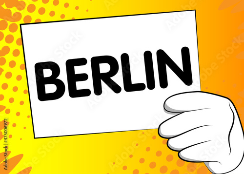 Cartoon Hand holding banner with Berlin text on white paper. Man showing billboard.