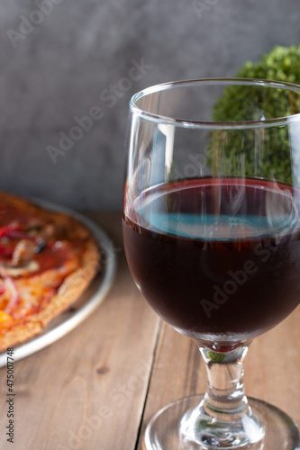 A closeup view of a glass of red wine, next to a pizza pie.