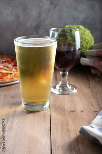 A view of a beer glass and wine glass next to a pizza.