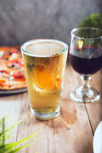 A view of a beer glass and wine glass next to a pizza.
