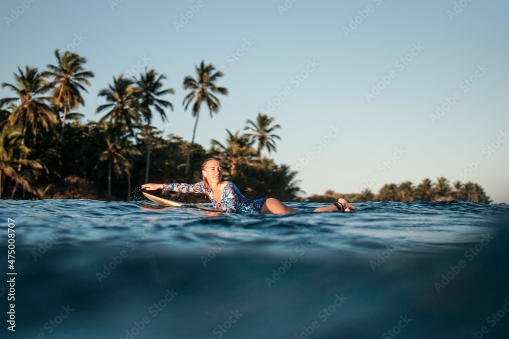 Portrait of blond surfer girl on white surf board in blue ocean pictured from the water in Encuentro beach