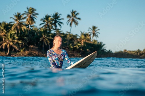 Portrait of blond surfer girl on white surf board in blue ocean pictured from the water in Encuentro beach © Lila Koan