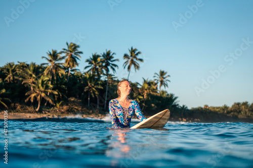 Portrait of blond surfer girl on white surf board in blue ocean pictured from the water in Encuentro beach