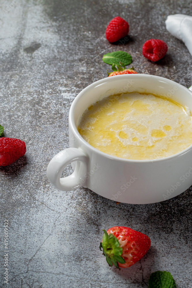 Cream of wheat, semolina pudding with butter and fresh raspberries and strawberries with mint in a white cup against a gray stone table. A healthy breakfast in a restaurant Cream of wheat, semolina pudding with butter and fresh raspberries and strawberries with mint in a white cup against a gray stone table. A healthy breakfast in a restaurant