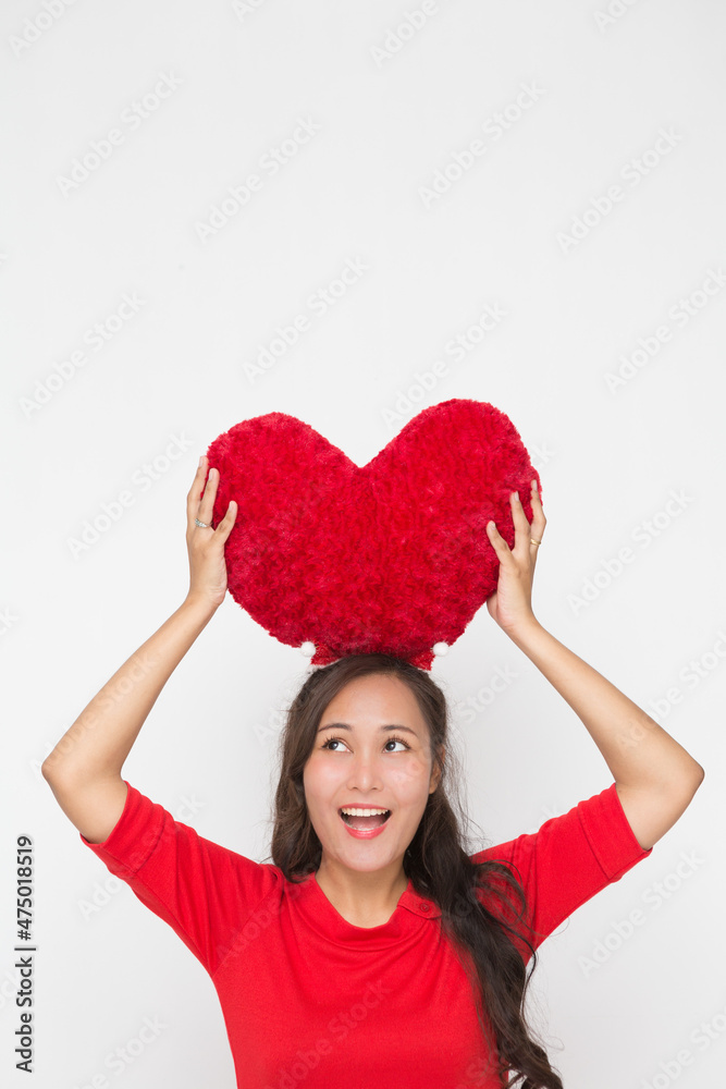 Beautiful Asian woman wearing small Santa hat and wearing red dress holding red heart shape pillow on white background Beautiful Asian woman wearing small Santa hat and wearing red dress holding red heart shape pillow on white background