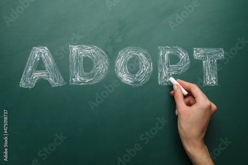 Woman with chalk writing word Adopt on board, closeup photo