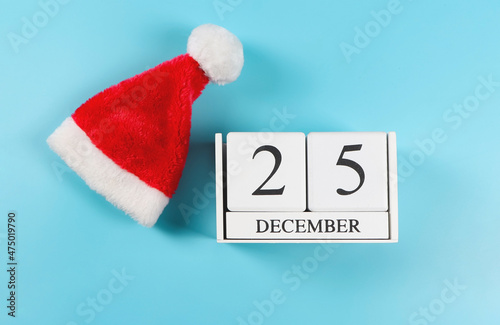 flat lay of wooden calendar December 25 with bright red Santa Claus hat on blue backgroud. Christmas background.