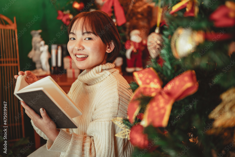 a young Woman in front of Christmas tree reading a book at home with x-mas decoration. a young Woman in front of Christmas tree reading a book at home with x-mas decoration.