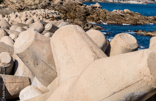 Closeup of tetrapod breakwater with craggy coastline in background.