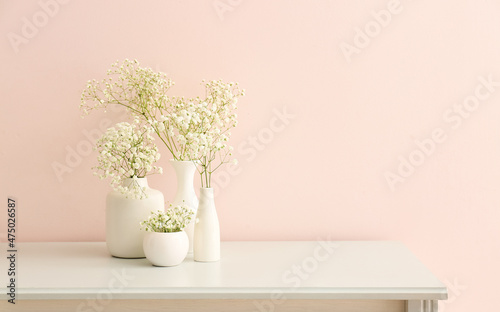 Vases with beautiful gypsophila flowers on table near light wall