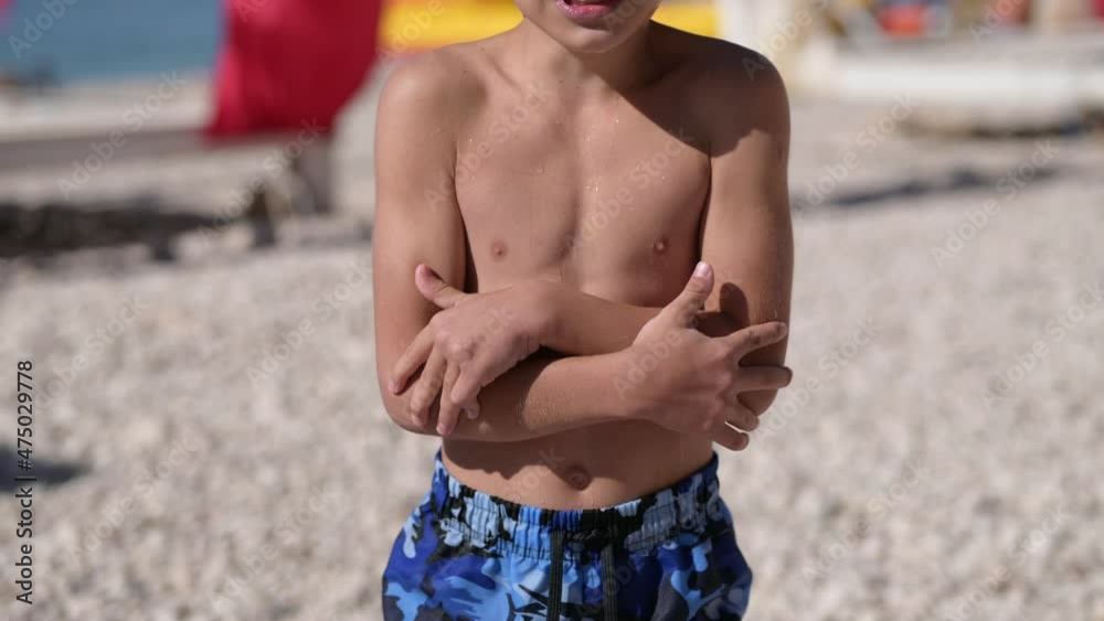 one little freeze boy in swimming trunks shorts shivering from cold on summer sea beach
