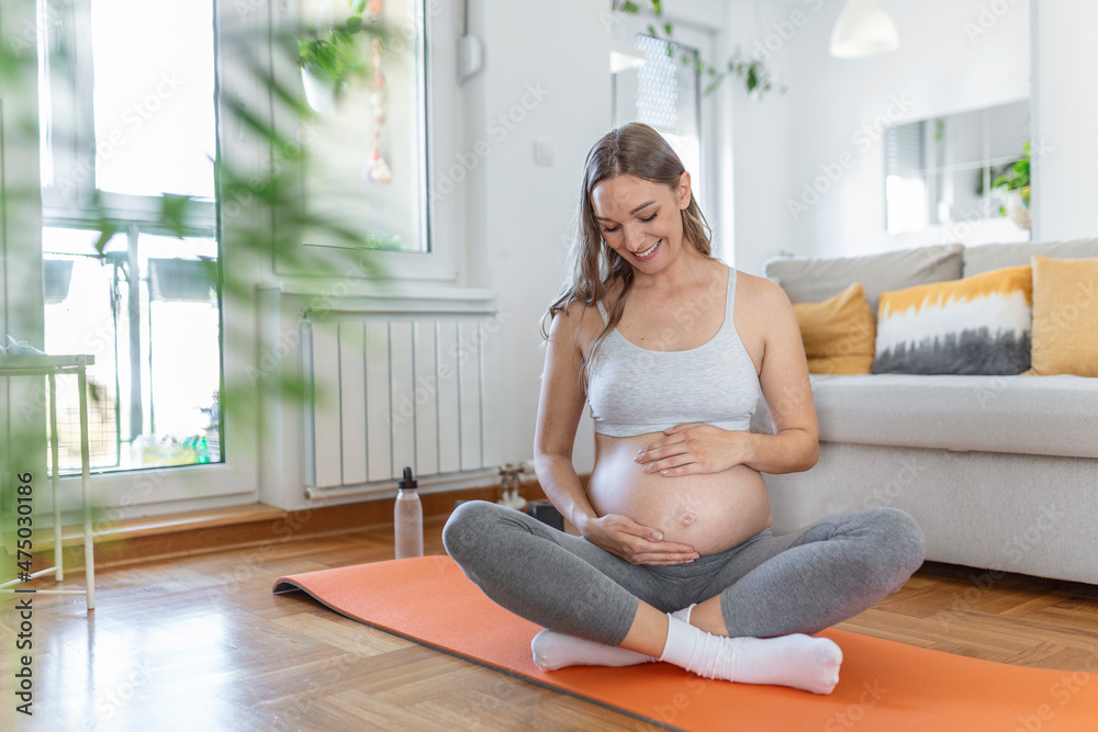 Close-up of pregnant woman touching her belly while sitting in lotus position