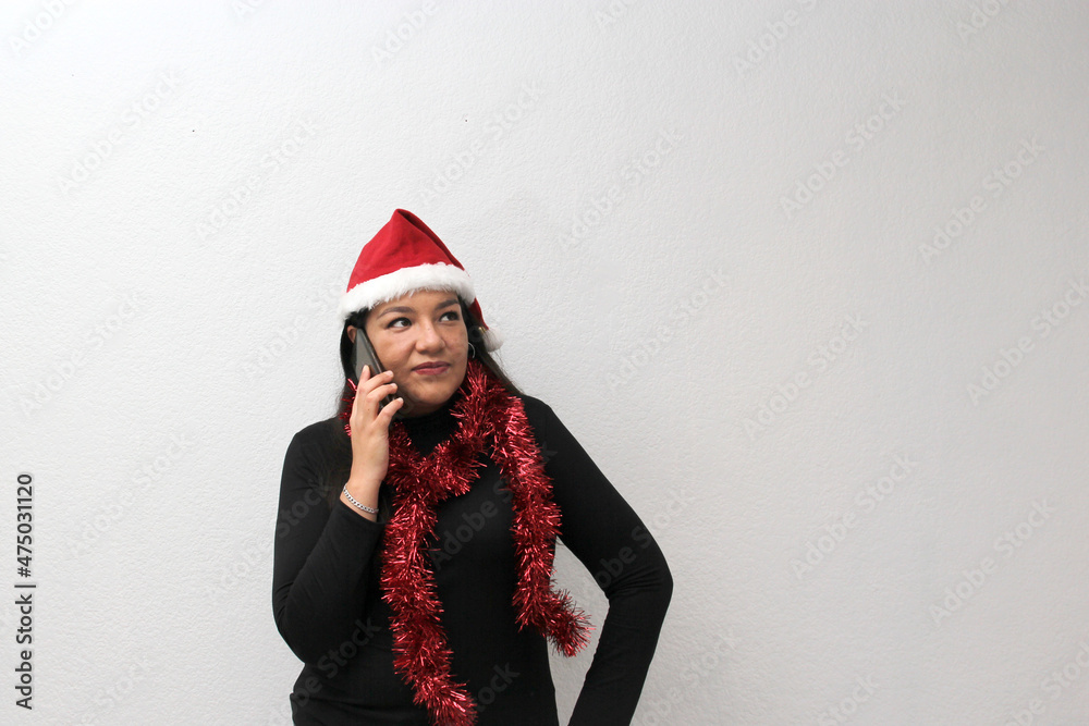 Latin adult woman with Christmas hat and red garland as scarf shows her cell phone that she uses for contests, promotions, calling her family with a video call happy and excited to celebrate Christmas Latin adult woman with Christmas hat and red garland as scarf shows her cell phone that she uses for contests, promotions, calling her family with a video call happy and excited to celebrate Christmas