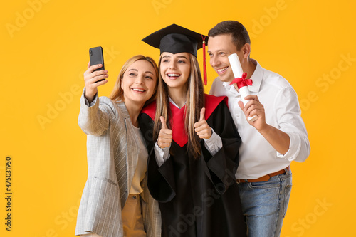 Happy female graduation student with her parents taking selfie on color background photo