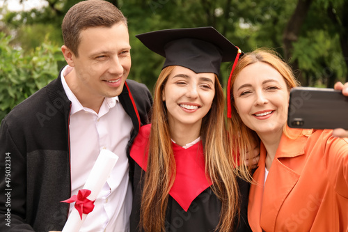 Happy young woman with her parents taking selfie on graduation day photo