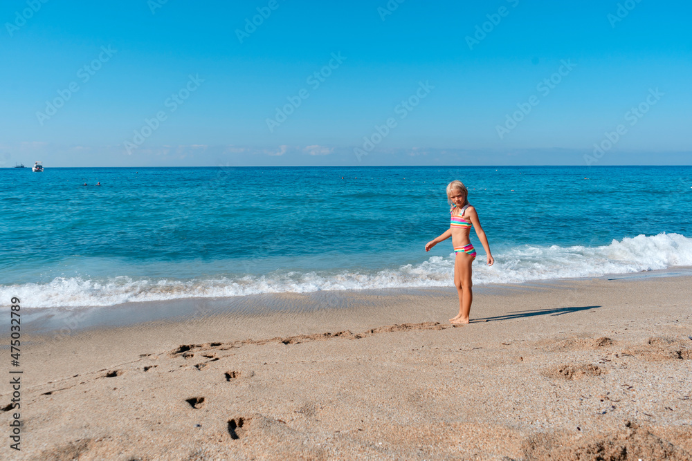 Blond preschool girl wearing colorful swimsuit near the sea on the sand beach on a beautiful summer sunny day. Blond preschool girl wearing colorful swimsuit near the sea on the sand beach on a beautiful summer sunny day.