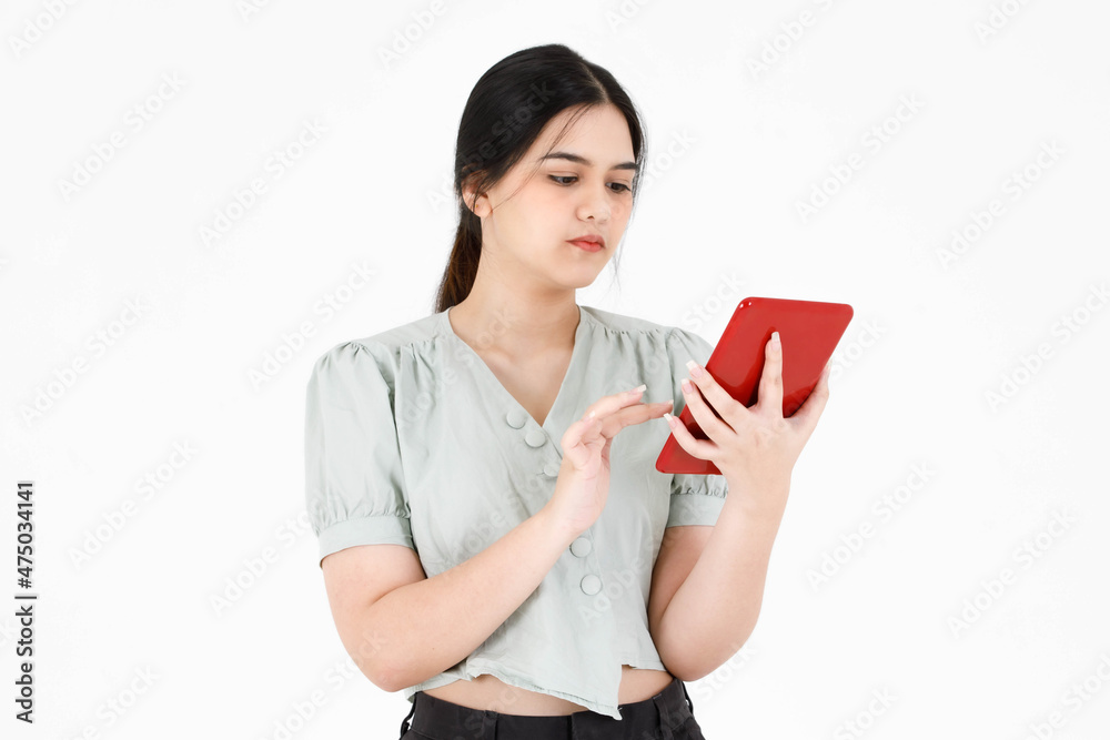 Studio shot of Asian young beautiful teenager female model with ponytail hairstyle wearing casual crop top outfit standing holding using touching touchscreen tablet in red case on white background Studio shot of Asian young beautiful teenager female model with ponytail hairstyle wearing casual crop top outfit standing holding using touching touchscreen tablet in red case on white background