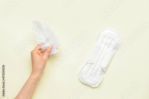 Female hand with feather and menstrual pad on yellow background