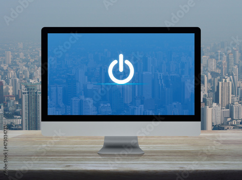 Power button icon on desktop modern computer monitor screen on wooden table over office building tower and skyscraper in city, Business start up online concept