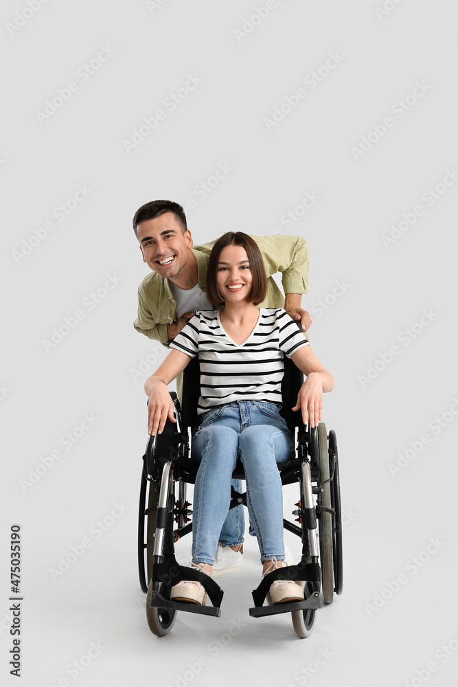 Young woman in wheelchair and her husband on light background Young woman in wheelchair and her husband on light background