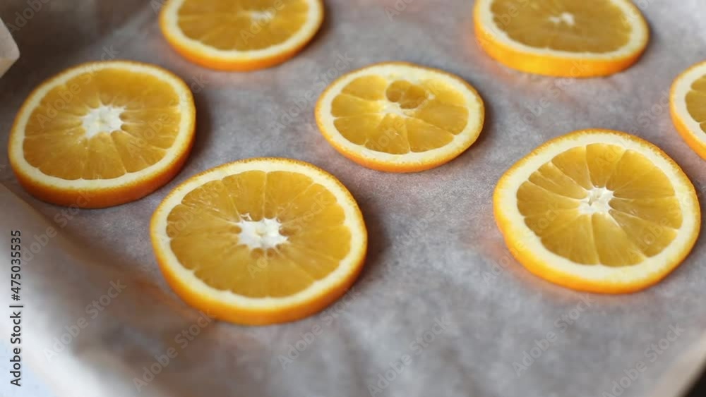 Oranges on a dish prepared for drying. The hand is placing the citrus slices on the baking paper. Bright juicy orange slices. Fruit Oranges on a dish prepared for drying. The hand is placing the citrus slices on the baking paper. Bright juicy orange slices. Fruit