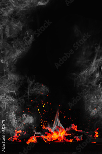 Fire flames and glowing coals on grill on black background with sparks and white smoke