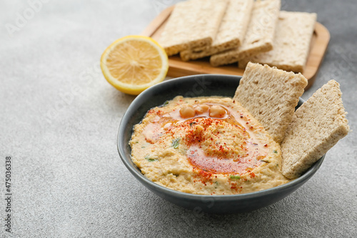 Bowl with delicious hummus and crackers on grey background, closeup