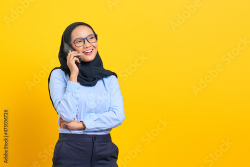 Portrait of happy young Asian woman talking on mobile phone and looking aside isolated on yellow background © Sewupari Studio
