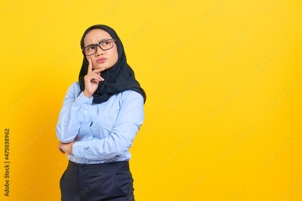 Portrait of pensive young Asian woman looking seriously thinking about a question isolated on yellow background