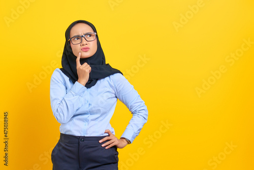 Portrait of pensive young Asian woman looking seriously thinking about a question isolated on yellow background © Sewupari Studio