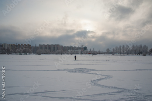 A lonely fisherman stands on a frozen pond