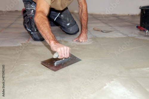 Construction worker leveling compound with putty knife. Renovation, floor leveling screed, mass distribution. Preparation for an even floor to installing a new vinyl as a floor covering in the kitchen